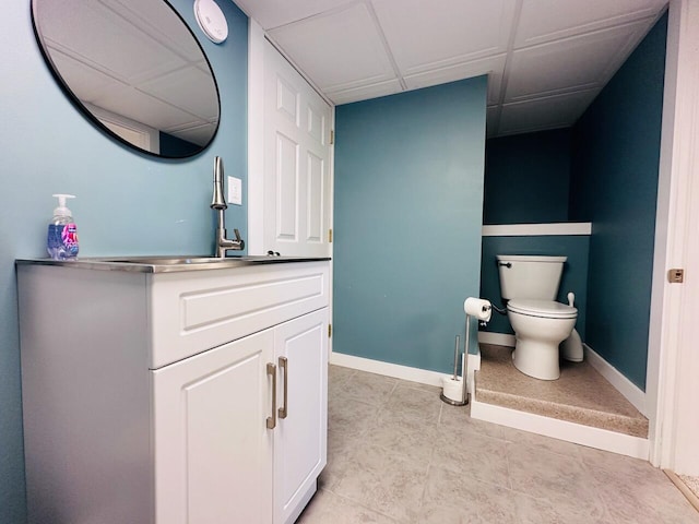 bathroom with baseboards, a sink, a drop ceiling, and toilet