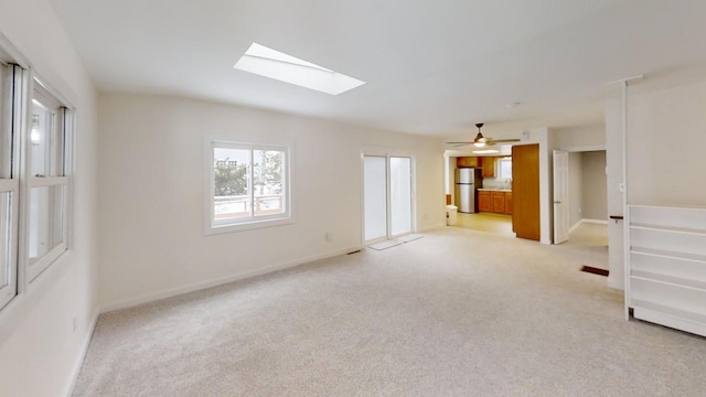 unfurnished room featuring a skylight, light colored carpet, and baseboards