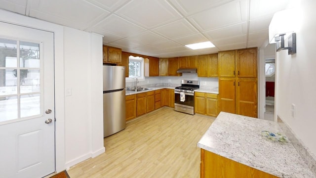 kitchen with light wood finished floors, brown cabinetry, stainless steel appliances, light countertops, and a sink