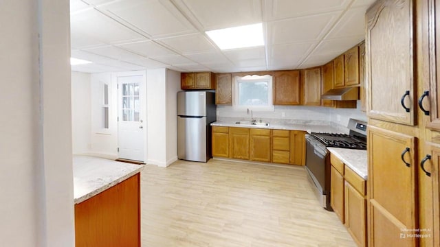 kitchen with stainless steel appliances, brown cabinets, a sink, and under cabinet range hood