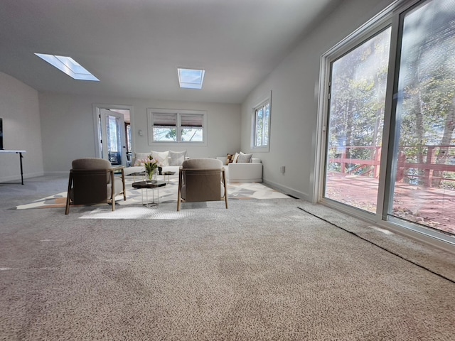 unfurnished living room featuring baseboards, vaulted ceiling with skylight, and light colored carpet