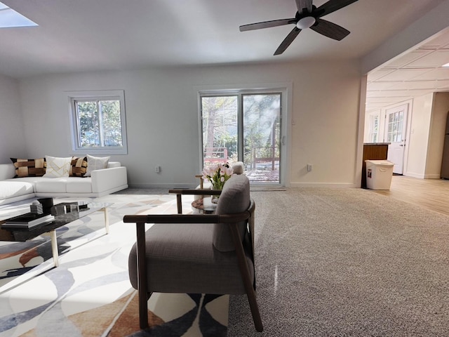 living area with a skylight, baseboards, a ceiling fan, and light colored carpet