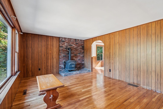 unfurnished living room featuring light hardwood / wood-style flooring, wooden walls, and a wood stove