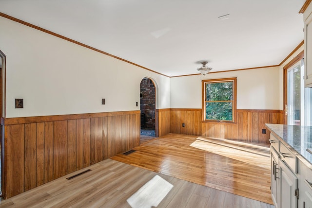 unfurnished living room featuring wood walls, light hardwood / wood-style floors, ornamental molding, and a healthy amount of sunlight