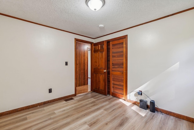 empty room featuring ornamental molding, light hardwood / wood-style floors, and a textured ceiling