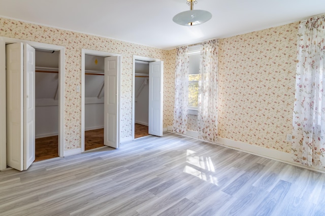 unfurnished bedroom with multiple closets and light wood-type flooring