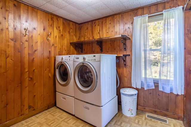 laundry room featuring wooden walls, washing machine and clothes dryer, and light parquet flooring