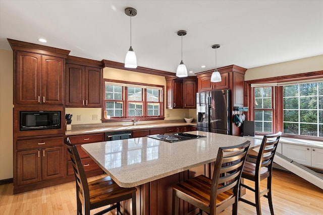 kitchen with a wealth of natural light, light hardwood / wood-style flooring, black microwave, and stainless steel fridge