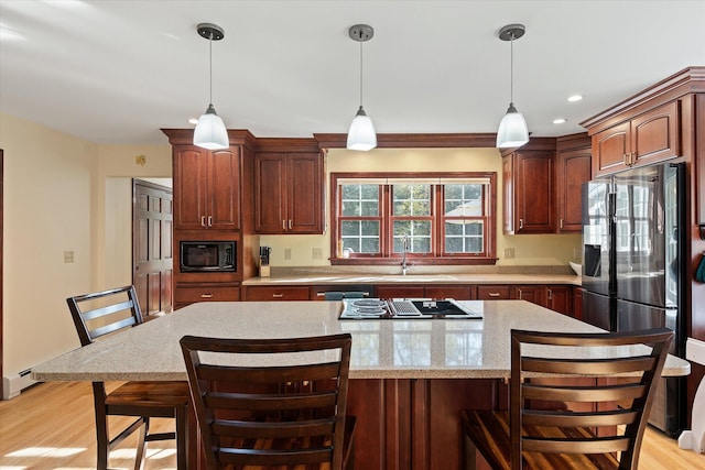 kitchen featuring light hardwood / wood-style floors, appliances with stainless steel finishes, decorative light fixtures, and a kitchen bar