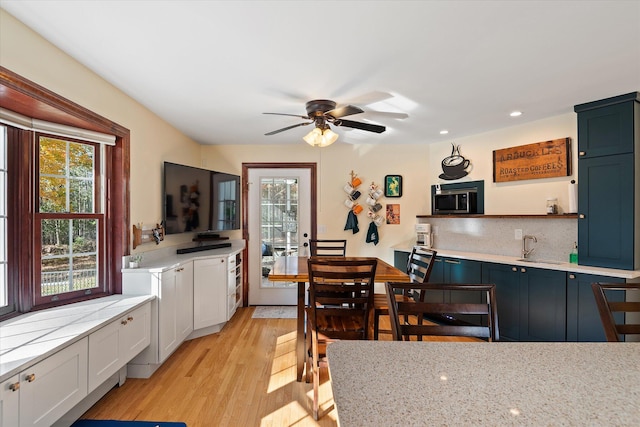 kitchen with blue cabinetry, light hardwood / wood-style flooring, light stone counters, and white cabinets