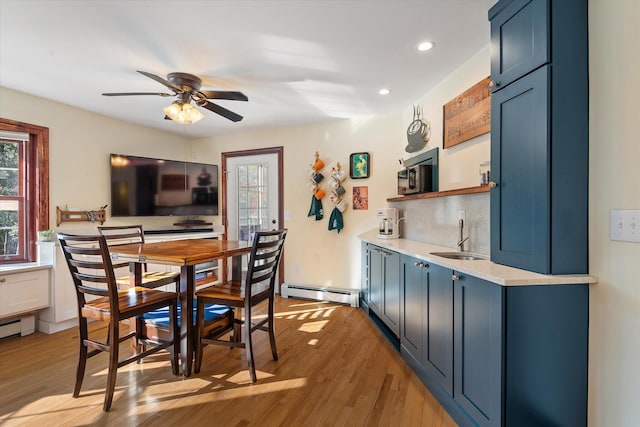 interior space with sink, ceiling fan, baseboard heating, blue cabinetry, and light hardwood / wood-style flooring