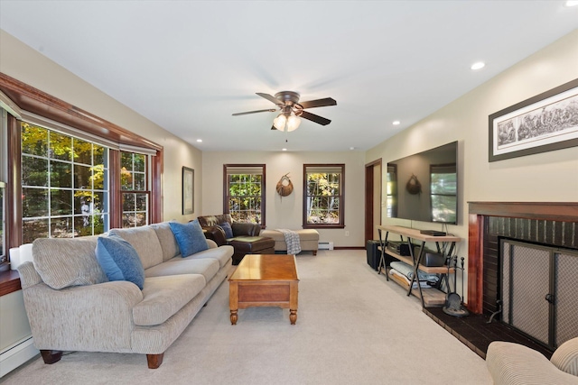 living room featuring a brick fireplace, a baseboard heating unit, light colored carpet, and ceiling fan