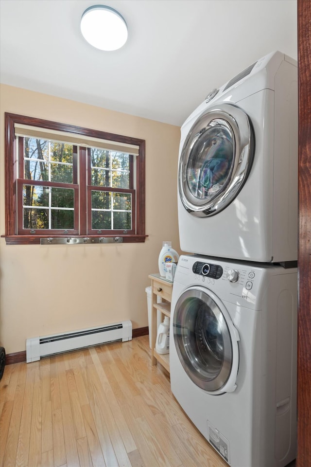 laundry area with a baseboard radiator, stacked washer / dryer, and light hardwood / wood-style flooring