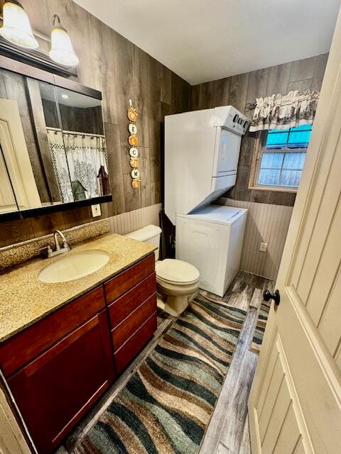 bathroom featuring stacked washing maching and dryer, vanity, hardwood / wood-style flooring, tile walls, and toilet