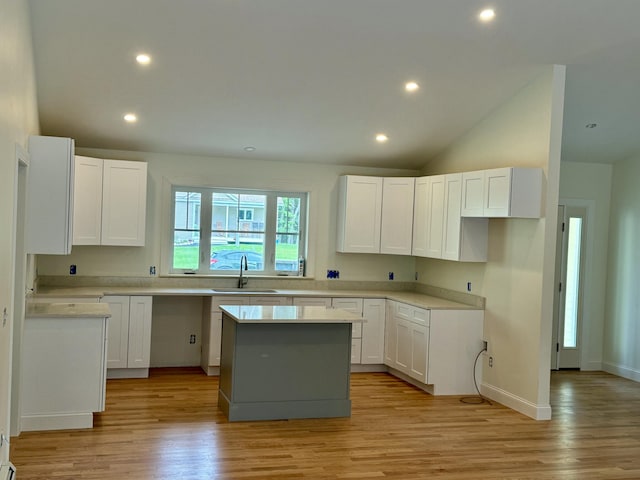 kitchen featuring light wood-style flooring, a sink, a center island, white cabinetry, and vaulted ceiling