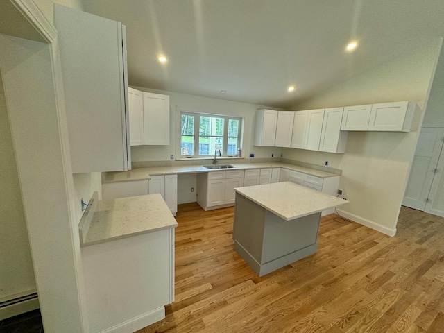 kitchen with a sink, a kitchen island, light wood-style floors, baseboard heating, and vaulted ceiling