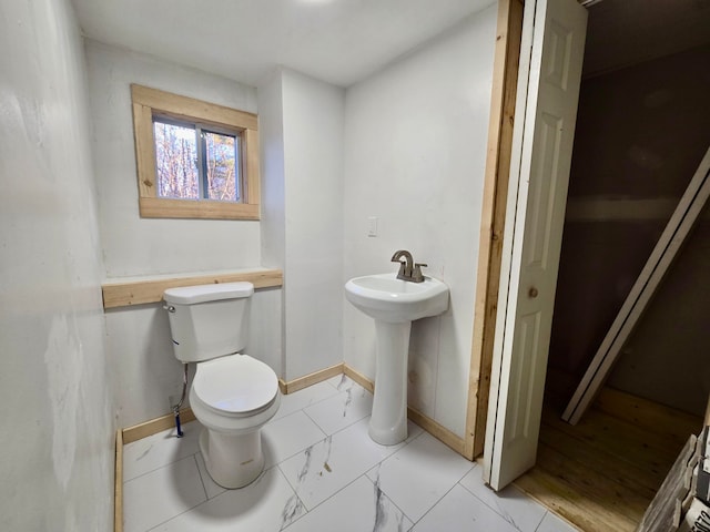 bathroom featuring marble finish floor, baseboards, a sink, and toilet