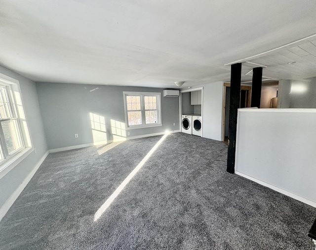 unfurnished living room featuring carpet floors, baseboards, a wall unit AC, and washing machine and clothes dryer