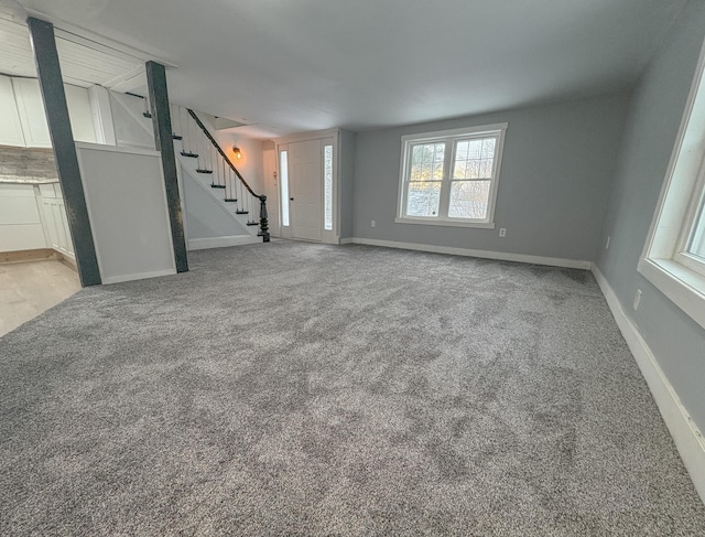 unfurnished living room with carpet, stairway, and baseboards