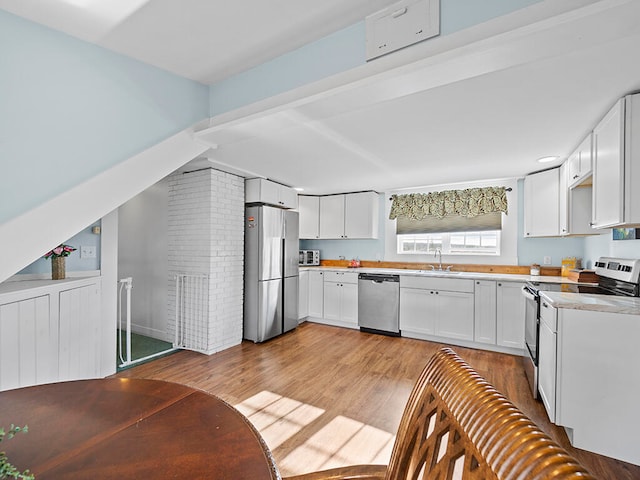 kitchen with white cabinets, sink, light wood-type flooring, stainless steel appliances, and brick wall