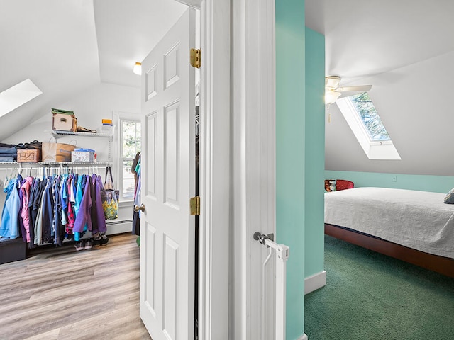 bedroom with ceiling fan, lofted ceiling with skylight, and light hardwood / wood-style flooring