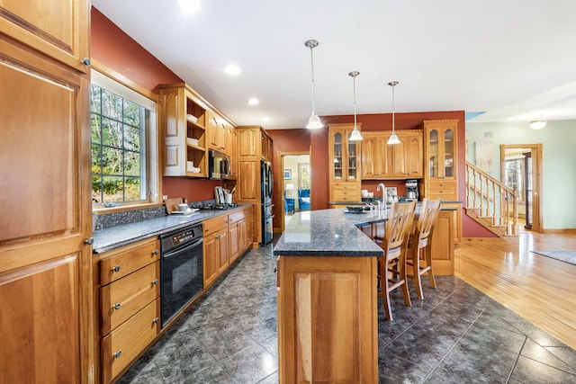 kitchen with dark hardwood / wood-style floors, a kitchen breakfast bar, hanging light fixtures, a center island with sink, and black appliances