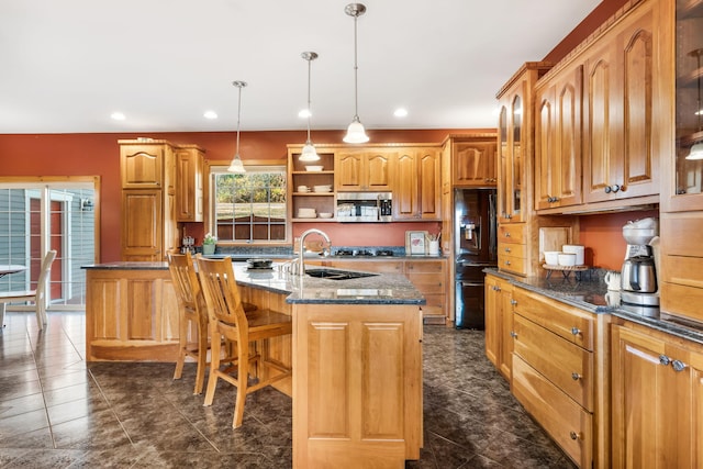 kitchen with a center island with sink, a breakfast bar area, black fridge, sink, and decorative light fixtures