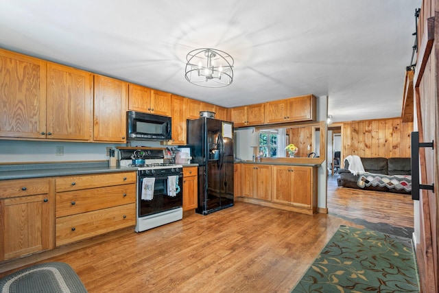 kitchen with black appliances, decorative light fixtures, a chandelier, light hardwood / wood-style floors, and wood walls