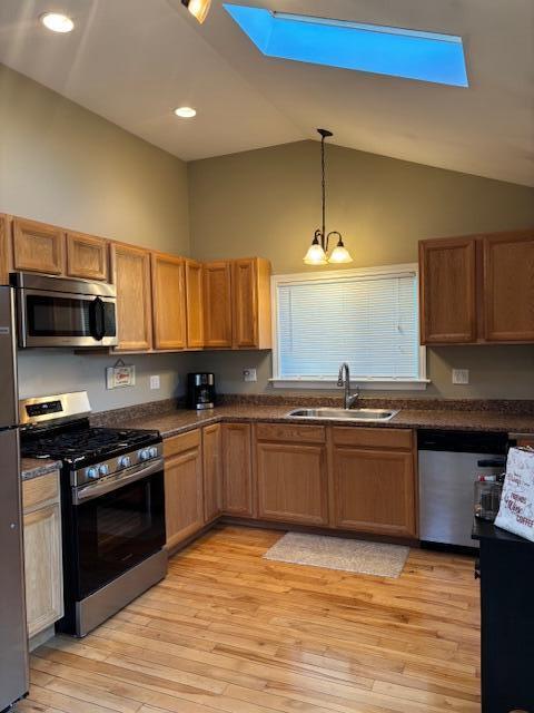 kitchen with appliances with stainless steel finishes, sink, pendant lighting, an inviting chandelier, and light hardwood / wood-style floors