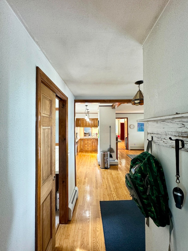 corridor with a textured ceiling, a baseboard heating unit, plenty of natural light, and hardwood / wood-style floors