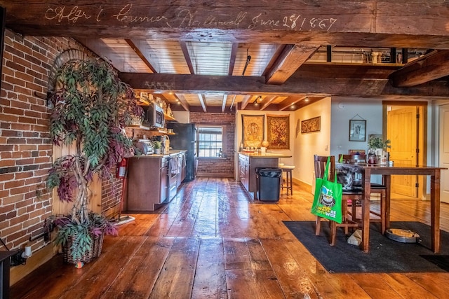 interior space featuring a kitchen island, black fridge, beamed ceiling, brick wall, and hardwood / wood-style floors