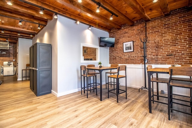 dining room with beam ceiling, brick wall, light hardwood / wood-style floors, and rail lighting