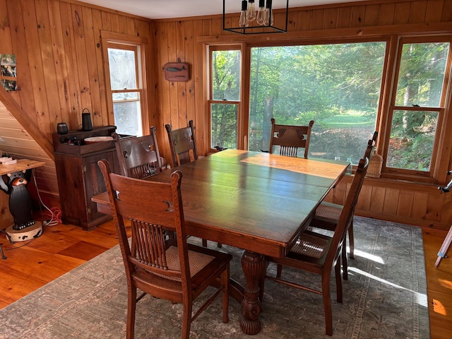 dining space with an inviting chandelier, wood walls, and dark wood-type flooring