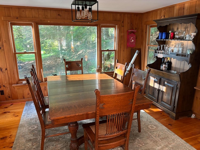 dining room with wood walls, wood-type flooring, and a chandelier