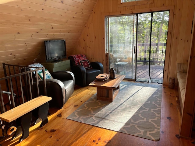 living room with light hardwood / wood-style flooring, wood walls, and vaulted ceiling