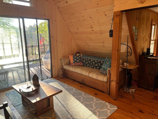 living room with wooden walls, vaulted ceiling, wood-type flooring, and a healthy amount of sunlight