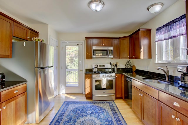 kitchen with light hardwood / wood-style floors, dark stone counters, sink, and stainless steel appliances