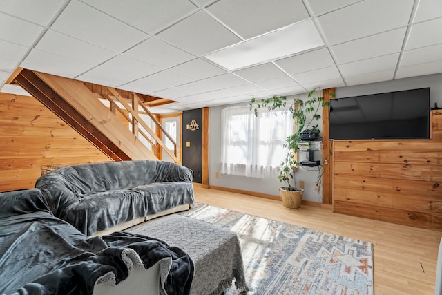 living room with hardwood / wood-style floors, a paneled ceiling, and wood walls