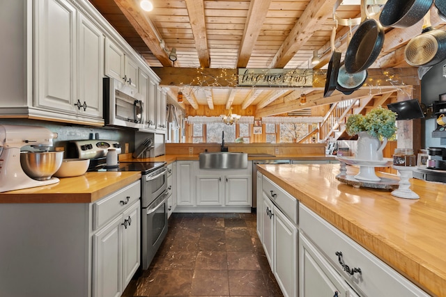 kitchen with white cabinets, appliances with stainless steel finishes, butcher block counters, sink, and beam ceiling