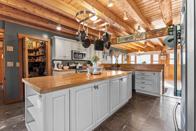 kitchen featuring a kitchen island, white cabinetry, stainless steel appliances, beamed ceiling, and butcher block countertops