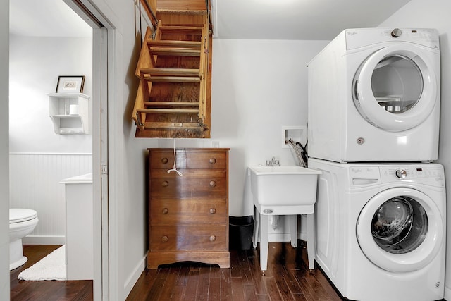 laundry room featuring wooden walls, sink, stacked washing maching and dryer, and dark hardwood / wood-style floors