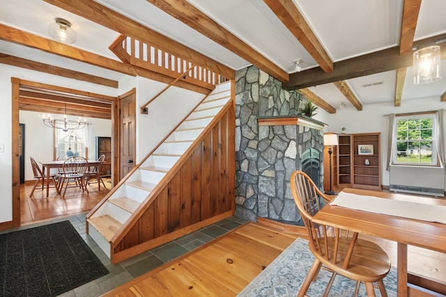 stairs with a stone fireplace, an inviting chandelier, hardwood / wood-style floors, and beam ceiling