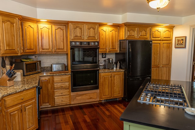 kitchen with dark stone countertops, backsplash, dark wood-type flooring, and black appliances