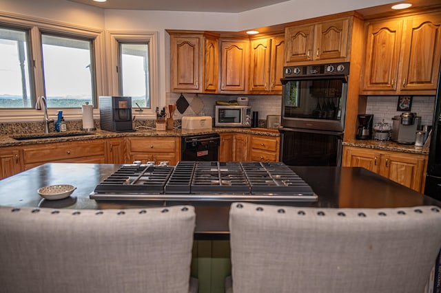 kitchen featuring dark stone counters, backsplash, sink, and black double oven