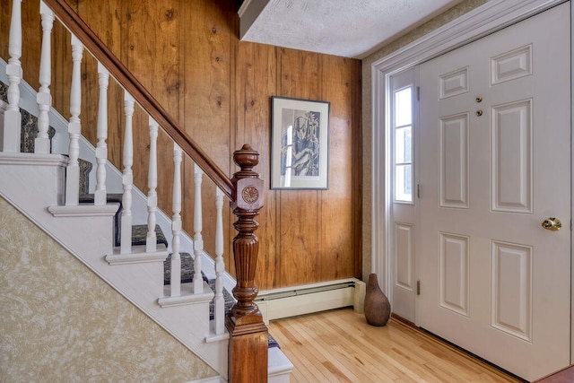 entrance foyer featuring wood walls, baseboard heating, a textured ceiling, and light wood-type flooring