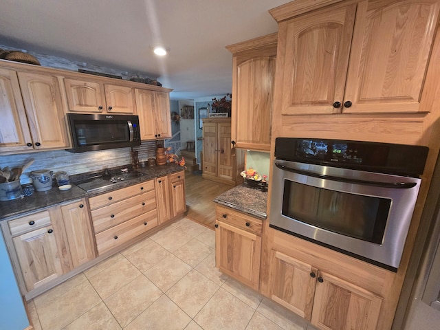 kitchen with black appliances, tasteful backsplash, light tile patterned floors, and dark stone countertops