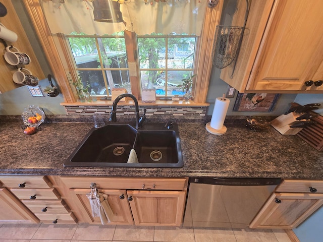 kitchen featuring stainless steel dishwasher, sink, dark stone counters, and light tile patterned floors