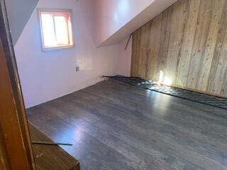 bonus room with dark wood-type flooring and wood walls