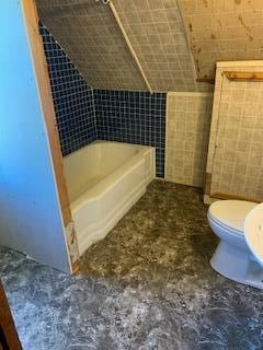 bathroom featuring toilet, a bathtub, and tile walls