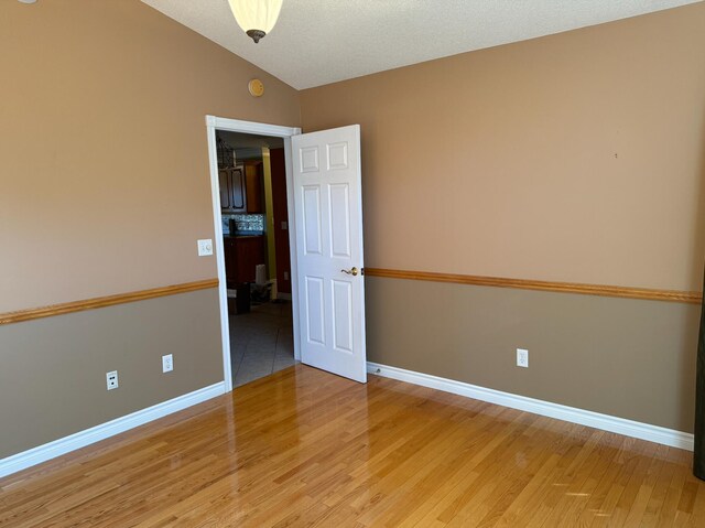 unfurnished room with a textured ceiling, wood-type flooring, and vaulted ceiling